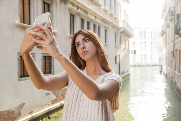 Femme rousse élégant prenant selfie avec canal vénitien sur fond flou — Photo de stock