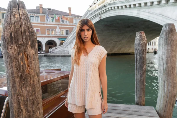 Femme en pull sans manches et short près des pilotis en bois sur le Grand Canal à Venise — Photo de stock