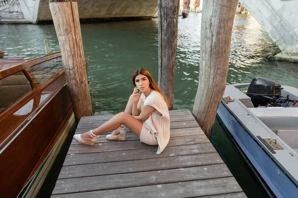 Hochwinkelaufnahme einer Frau in sommerlicher Strickbekleidung, die auf einem hölzernen Pier in Venedig sitzt — Stockfoto