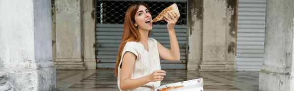 Happy woman in sleeveless jumper eating delicious pizza on street in Venice, banner — Stock Photo