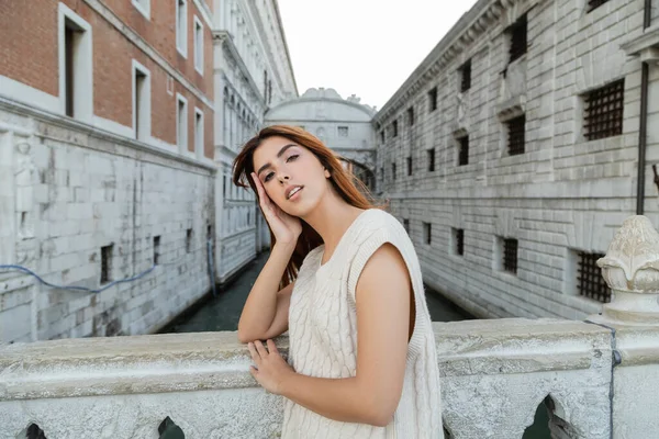 Молодая женщина с рукой возле забора смотрит в камеру возле средневековой тюрьмы в Венеции — стоковое фото