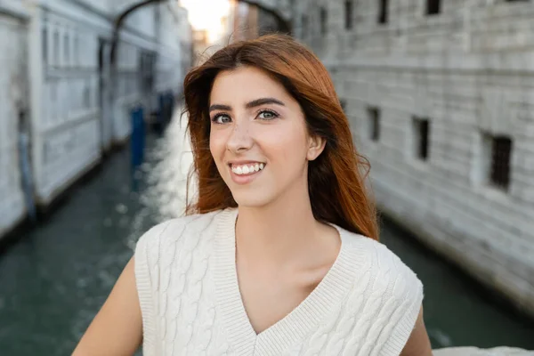 Portrait de jeune femme heureuse aux cheveux roux souriant à la caméra à Venise sur fond flou — Photo de stock