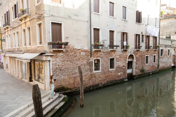 Young woman in dress standing near buildings and canal on medieval street in Venice — Stock Photo