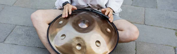 Обрезанный вид человека, играющего на висячем барабане на городской улице, баннер — стоковое фото