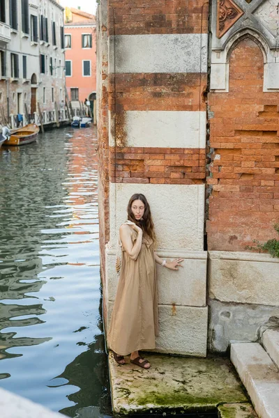 Femme enceinte en robe tenant un sac à ficelle près de la rivière et du bâtiment à Venise — Photo de stock