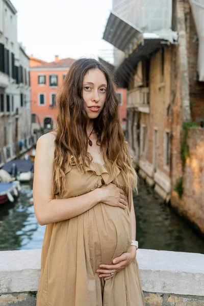 Portrait of pregnant woman in dress looking at camera in blurred Venice — Stock Photo