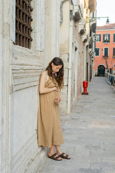 Jeune femme enceinte en robe touchant le ventre dans la rue urbaine en Italie — Photo de stock