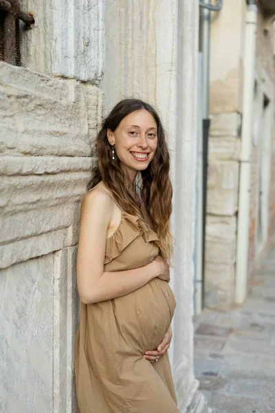 Joyeux femme enceinte regardant caméra oreille vieux bâtiment en Italie — Photo de stock