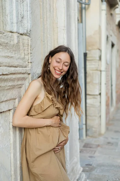 Mujer embarazada con los ojos cerrados de pie en la calle urbana de Venecia - foto de stock