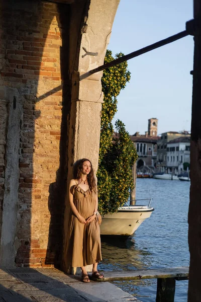 Cheerful pregnant woman standing in arch near pier in Venice — Photo de stock
