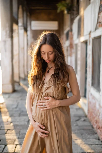 Portrait of pregnant woman touching belly near blurred old building in Venice — Stockfoto