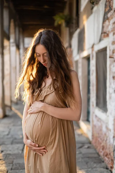 Stilvolle Schwangere berührt Bauch auf urbaner Straße in Venedig — Stockfoto