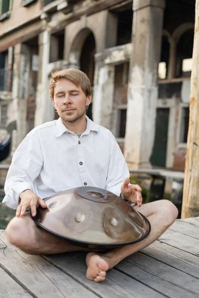 Musicien les yeux fermés jouant du tambour suspendu sur une jetée en bois à Venise — Photo de stock