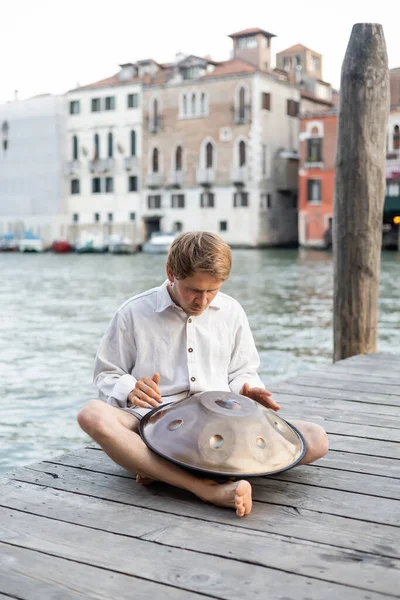 Musicien pieds nus jouant du tambour suspendu sur la jetée près de la rivière à Venise — Photo de stock