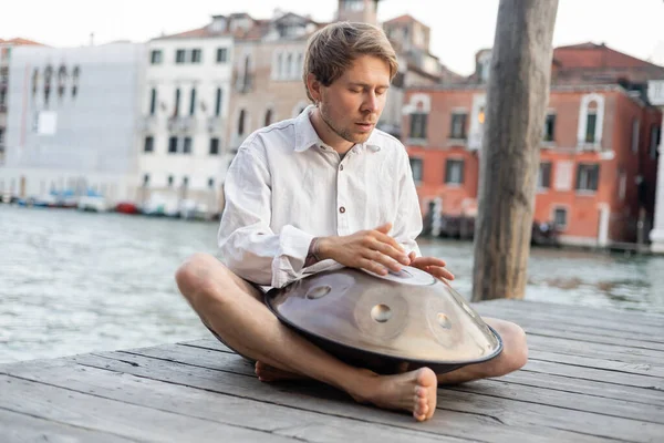 Músico com olhos fechados se apresentando em handpan no cais de madeira na Itália — Fotografia de Stock