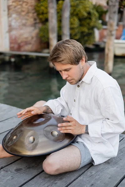 Tattooed musician playing handpan on pier in Italy — Stock Photo