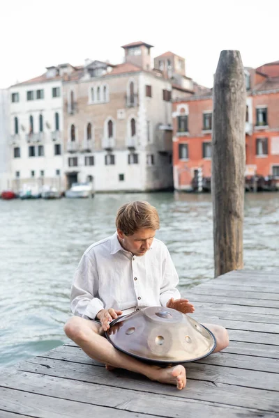 Homme pieds nus jouant du tambour suspendu sur une jetée en bois à Venise — Photo de stock