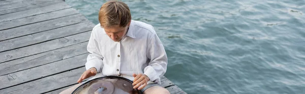 Man performing on hang drum on pier above river in Venice, banner — Photo de stock