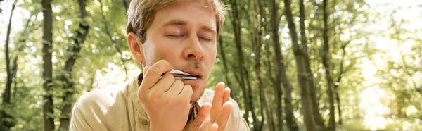 Man playing jews harp in blurred forest, banner — Stock Photo