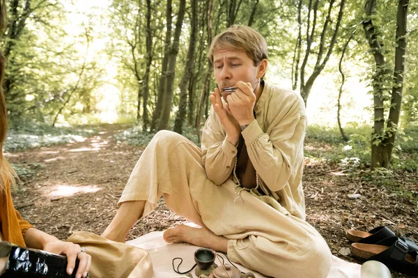 Barefoot man playing jews harp near wife in forest — Stock Photo