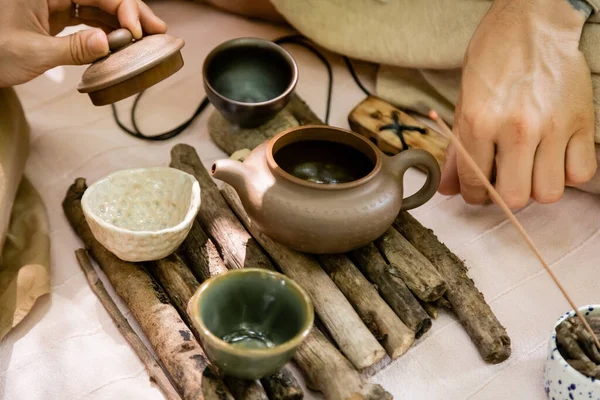 Vista recortada de la mujer sosteniendo la tapa de la tetera cerca de tazones de té y el marido al aire libre - foto de stock