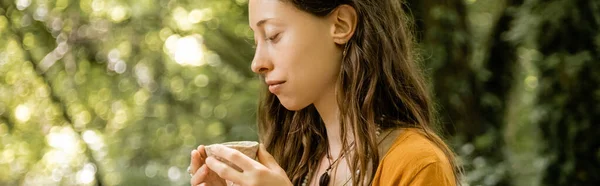 Side view of brunette woman holding tea bowl in summer forest, banner — Stockfoto