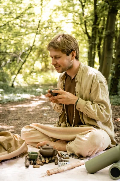 Uomo con gli occhi chiusi che tiene ciotola durante la cerimonia del tè nella foresta — Foto stock