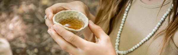 Cropped view of woman holding bowl with tea in forest, banner — Photo de stock