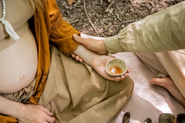 Cropped view of man touching hand of pregnant wife holding tea bowl in forest — Stock Photo