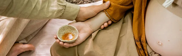 Cropped view of man touching pregnant wife during tea ceremony in forest, banner — Stock Photo