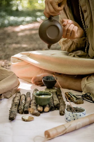 Обрезанный вид человека, наливающего чай в миску возле Варгана на одеяло в лесу — стоковое фото