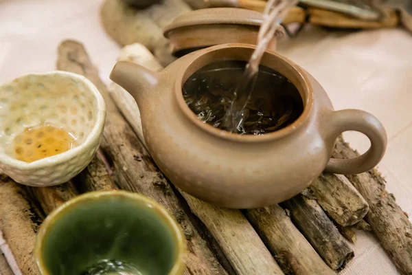 L'eau coulant dans la théière près des bols sur la planche en bois à l'extérieur — Photo de stock