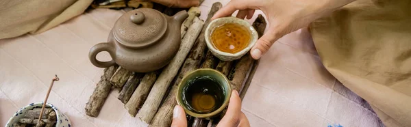 Vista recortada de la pareja sosteniendo tazones con té durante la ceremonia del té al aire libre, pancarta - foto de stock