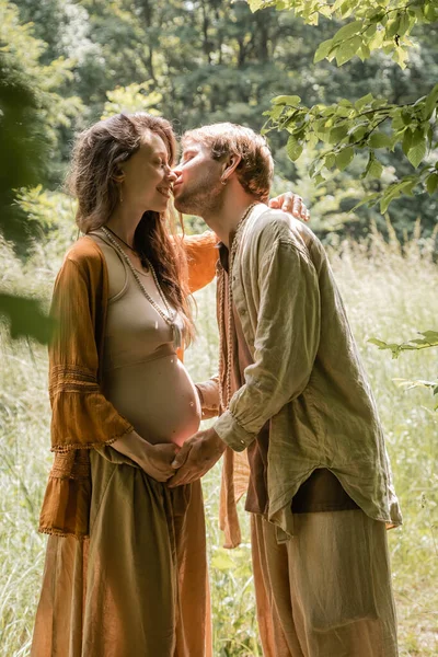 Vue latérale de l'homme embrassant souriant femme enceinte dans la forêt — Photo de stock