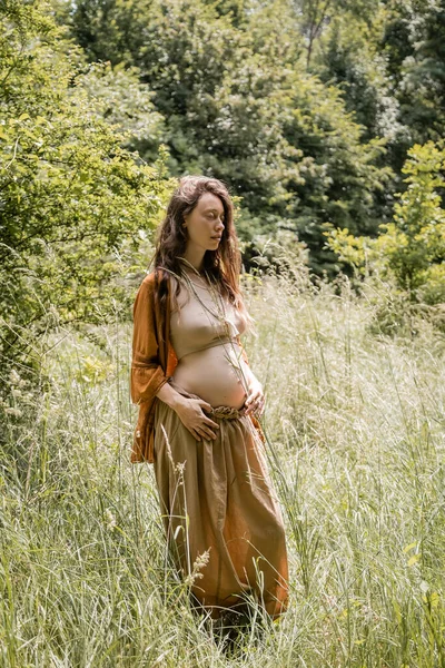 Беременная женщина закрывает глаза, стоя в поле — стоковое фото