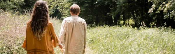 Back view of couple holding hands while walking on summer field, banner — Fotografia de Stock