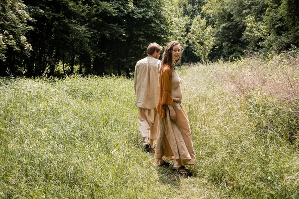 Smiling pregnant woman looking at camera near husband in summer field — Stock Photo