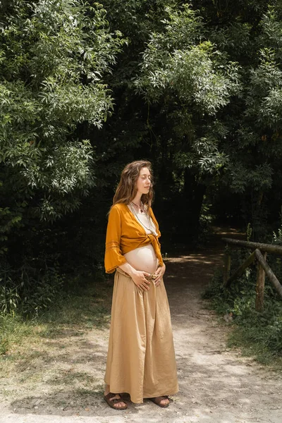 Беременная женщина стоит на дорожке в летнем лесу — стоковое фото
