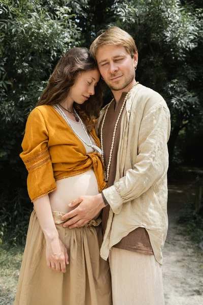 Man with closed eyes touching pregnant wife in forest — Stock Photo