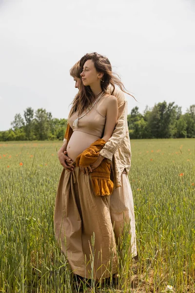 Vue latérale de l'homme embrassant femme enceinte dans le champ — Photo de stock