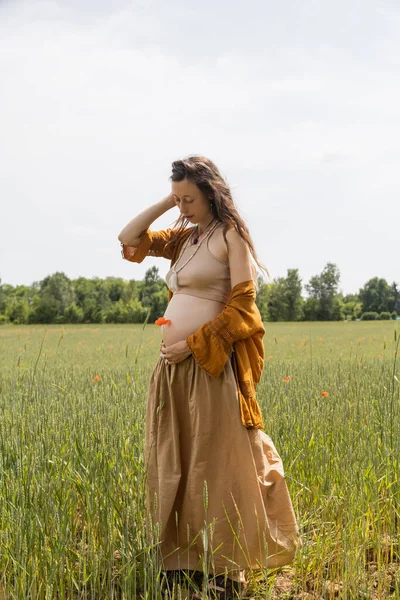 Mulher grávida segurando pappy flor enquanto em pé no campo — Fotografia de Stock