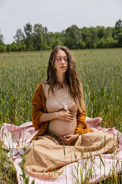 Young pregnant woman sitting on blanket in summer field — Photo de stock