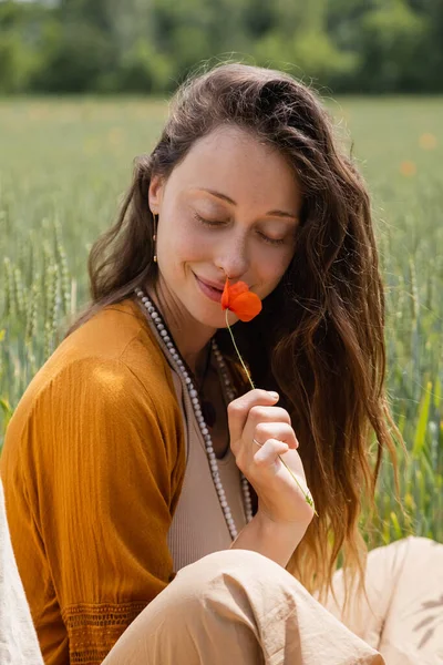 Sorrindo jovem mulher cheirando flor de papoula no campo — Fotografia de Stock