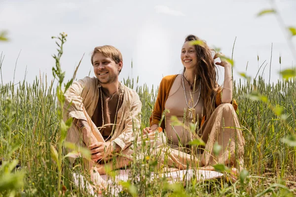 Cheerful pregnant woman sitting on blanket near husband in field — Stock Photo