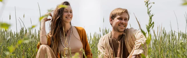 Positive couple sitting near grass in field, banner — Photo de stock