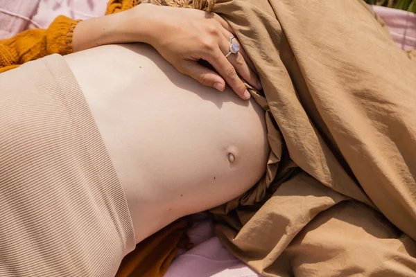 Обрізаний вид вагітної жінки відпочиває на ковдрі на відкритому повітрі — стокове фото
