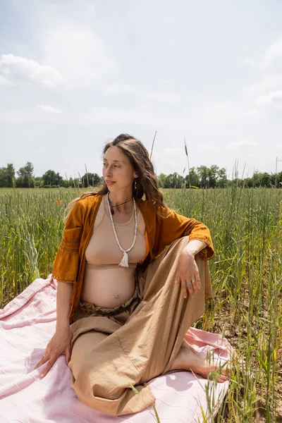 Femme enceinte souriante assise sur une couverture dans un champ — Photo de stock