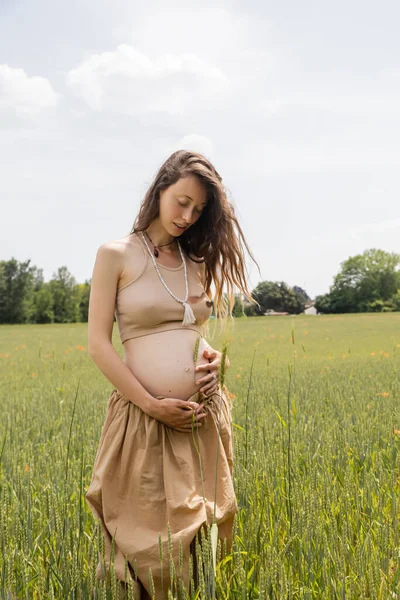 Pregnant woman holding spikelet near belly in summer field — Stock Photo