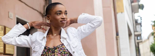 Stylish african american woman touching neck and looking away on urban street, banner — Stock Photo