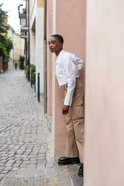 Fashionable african american woman standing near building on urban street in Treviso — Stock Photo
